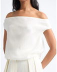 An off-the-shoulder white blouse with a soft, draped fabric and short cap sleeves, shown on a model against a plain white background.