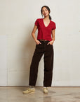 Person wearing a red top and brown pants standing against a white wall. front view