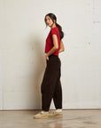 Woman wearing a red top and dark pants against a white wall side view