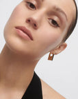Close-up of a person wearing a gold earring on a plain background