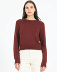 Woman wearing a burgundy sweater and white pants on a white background