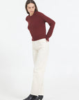 Woman wearing a burgundy sweater and white pants on a white background