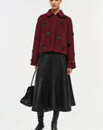 Woman wearing a burgundy coat with black embellishments and a black leather skirt on a white background
