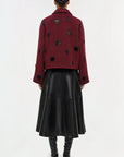 Person wearing a burgundy coat with black polka dots and a black leather skirt on a white background