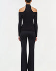 Person wearing a black outfit with a high neckline and flared pants on a white background back