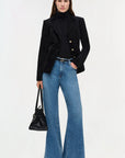 Woman wearing a black blazer, blue jeans, and holding a black handbag on a white background