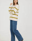Woman wearing a cream sweater with yellow stripes and blue jeans on a white background