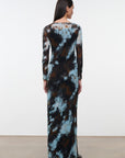 A woman viewed from the back wearing a long-sleeve maxi dress with a blue, brown, and black abstract tie-dye pattern, standing against a plain white studio wall.