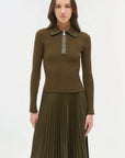 Woman wearing a brown/green ribbed sweater with a zipper and pleated skirt on a white background
