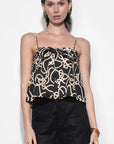Woman wearing a black and gold patterned top with black shorts on a white background