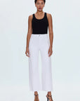 Woman wearing a black tank top and white pants on a light gray background