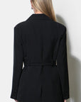A woman shown from the back wearing a black belted blazer and gray trousers against a plain light background.