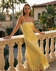 Woman in a yellow dress standing on a balcony with a tropical setting