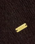 A close-up of dark brown textured fabric with a small rectangular gold-tone metal tag engraved
