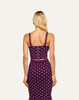 A woman viewed from the back wearing a purple and white polka dot two-piece set consisting of a crop top with shoulder straps and a matching high-waisted pencil skirt, against a solid off-white background.