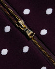 Close-up of a gold zipper on a dark purple fabric with white polka dots.