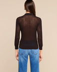 A woman viewed from the back wearing a dark brown sheer long-sleeve knit top and blue jeans, set against a solid beige studio background.
