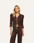 A woman modeling a dark brown cropped knit cardigan with textured sequins and puffed sleeves, paired with dark brown pants, against a solid off-white background.