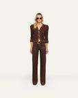 A model stands against a plain off-white studio background wearing a dark brown textured three-quarter sleeve jacket with puffed shoulders and matching dark brown wide-leg trousers.