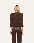 A woman viewed from the back wearing a dark brown textured knit cropped sweater with puffed shoulders and ribbed cuffs, paired with dark brown pants, against a plain off-white background.