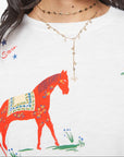 Woman wearing sunglasses and a white shirt with a colorful horse design on a plain background