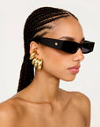 Woman wearing black sunglasses and gold hoop earrings on a light gray background