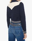 Woman wearing a navy and white sweater with a patterned belt and blue jeans on a white background