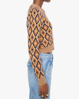 A side-profile view of a model wearing a cropped long-sleeve knit sweater with a geometric diamond pattern in tan, brown, and black, paired with light blue jeans against a plain white background.