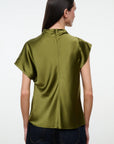 A woman viewed from the back wearing a short-sleeved olive green satin blouse and dark blue jeans against a plain white studio background.