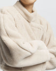 Close-up of a person wearing a beige fur coat with a plain background
