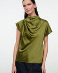 A woman modeling a short-sleeve olive green draped satin top with dark blue jeans, shot against a plain light gray studio background.