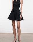 A model wearing a black halter-neck mini dress with a buttoned bodice and flared skirt, paired with black strappy high-heeled sandals, set against a plain white studio background.