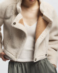 Person wearing a beige fleece jacket over a white top and gray pants on a light background