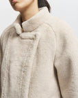 Close-up of a person wearing a beige coat with a neutral background, side view