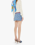 Woman wearing a colorful scarf, white sweater, and denim skirt on a white background