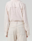 Person wearing a light cream shirt and beige pants against a gray background