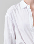 A close-up of a person wearing a white long-sleeve button-up shirt against a light gray background.