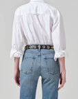 Person wearing a white shirt and blue jeans with a decorative belt on a plain background