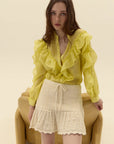 Woman wearing a yellow blouse and off-white knit skirt sitting on a beige chair.