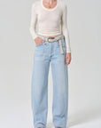 Person wearing light blue jeans and a cream long-sleeve top on a white background