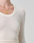 Person wearing a gold necklace with a pendant on a plain background