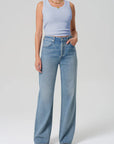 Person wearing a light blue sleeveless top and high-waisted jeans on a white background