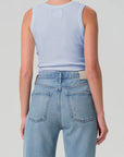 Person wearing a light blue sleeveless top and high-waisted jeans on a plain background