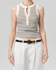 Person wearing a striped sleeveless top and white pants on a plain background