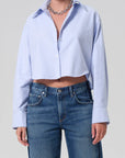 Person wearing a light blue button-up shirt and blue jeans on a plain background