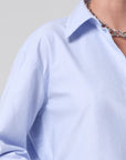 Close-up of a light blue shirt with a collar and a necklace on a neutral background