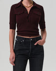 Person wearing a burgundy cropped shirt and black jeans on a plain background