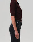Person wearing a maroon shirt and black pants on a plain background side view