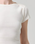 Close-up of a person wearing a short-sleeve waffle-knit top in a warm off-white or cream color, shown against a light gray studio background.