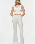 Woman wearing a white sleeveless top and high-waisted pants on a white background